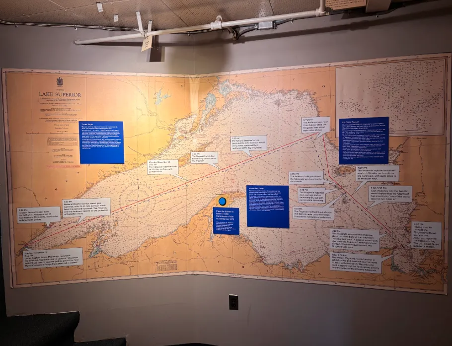 A nautical chart of Lake Superior enlarged and projected on a wall, with lines showing ships’ routes and  blue and white text bubbles pointing out important points in time on November 10, 1975